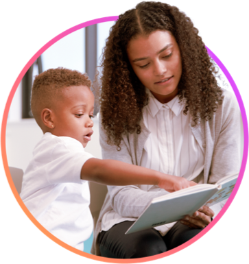 Teacher sitting and reading with a young boy, the student is pointing at the book