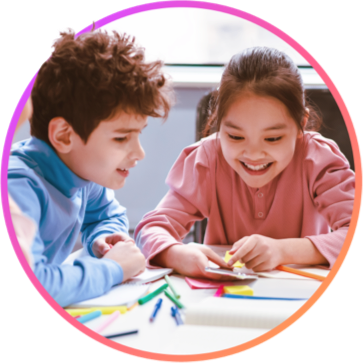 Two young students sitting together at a work table, smiling and learning together